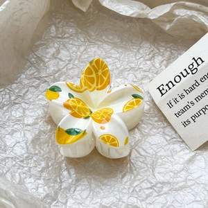 Macro view of plumeria hair claw clip with lemon print detail on soft beige paper