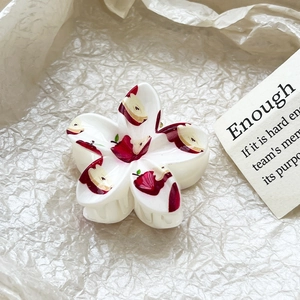 Close-up of a white flower hair claw with vibrant red apple print on creamy acetate material