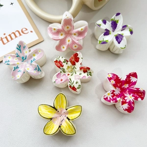 Detailed top view of six colorful UV printed plumeria flower hair claws on a textured surface