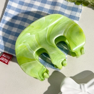 Détail d'une pince à cheveux en acétate vert marbré en forme de M sur tissu à carreaux