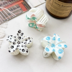 Close-up of resin hair claws featuring floral and cat paw prints on a white leather surface