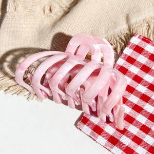 Macro shot of pink marble hair claw clip with golden metal spring on cozy fabric