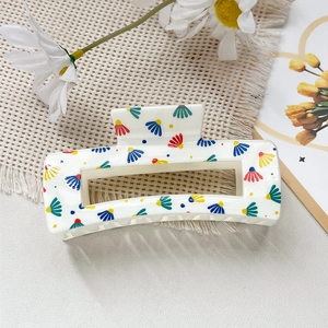 Détail de la pince à cheveux carrée avec motif floral coloré sur un tapis en osier tressé