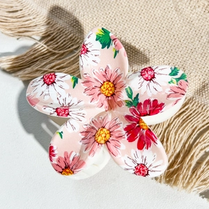 Detail of pink plumeria hair claw clip with floral patterns on beige woven mat