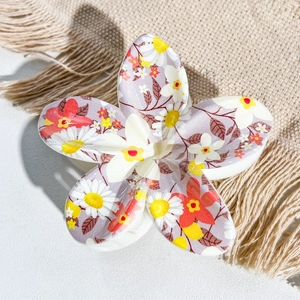 Detail shot of a floral print claw clip featuring red petals on a beige fringe fabric