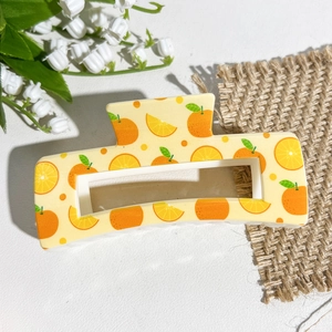 Détail de la pince à cheveux carrée avec imprimé orange et pois sur fond jaune clair