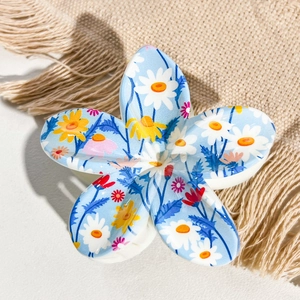 Detail shot of sky blue frangipani hair claw clip with daisy print on beige woven background