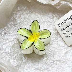 Detail showing lime green frangipani hair claw clip with yellow center on white paper