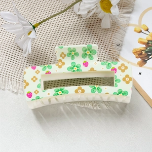 Détail d'une pince à cheveux crème avec motifs floraux verts et petites fraises