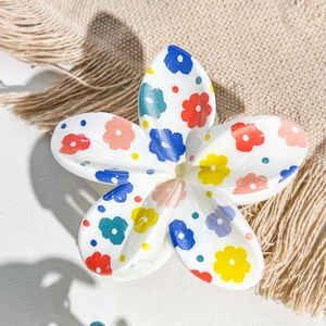 Detailed close-up of a floral print egg flower hair claw clip on a soft beige fabric