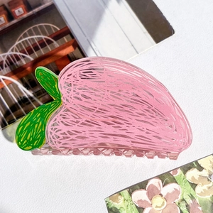 Gros plan d'une pince à cheveux en acrylique en forme de pêche rose avec détail de feuille
