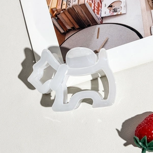 Close-up of white acetate dog-shaped hair claw clip on a textured background