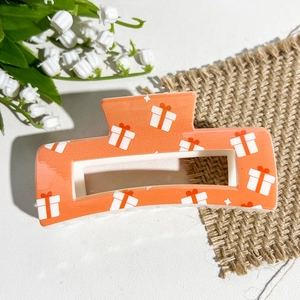 Vue détaillée d'une pince à cheveux orange rectangulaire avec motifs cadeaux sur textile