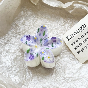 Close-up of frangipani hair claw clip with purple floral print on matte white surface
