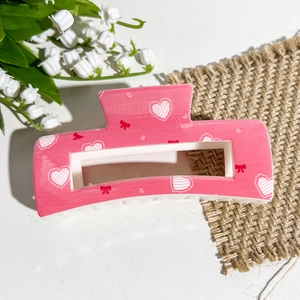Vue détaillée de la pince à cheveux rose rectangulaire avec motifs cœurs et nœuds