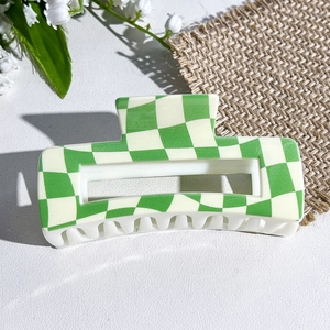 Close-up of green checkered square hair claw clip on white leather with lily of the valley