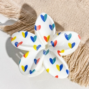 Close-up detail of white frangipani hair claw clip with colorful heart pattern print