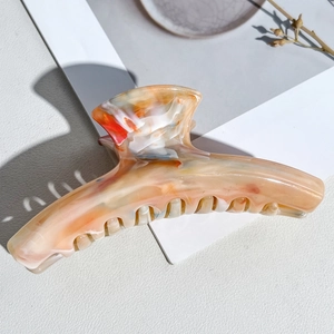 Detail of large acetate hair claw clip with beige marble texture and coral orange accents