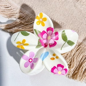 Detail view of Frangipani hair claw clip with floral UV print on beige textured fabric