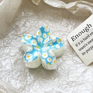 Close-up of a white plumeria flower hair claw clip with delicate blue daisy print