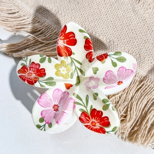 Macro shot of white flower hair claw with colorful floral UV print on beige fabric
