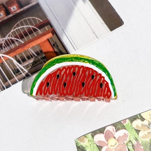 Détail d'une pince à cheveux en acrylique en forme de pastèque sur fond en tissu blanc