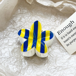 Close-up of blue and yellow striped frangipani hair claw clip on minimalist paper background