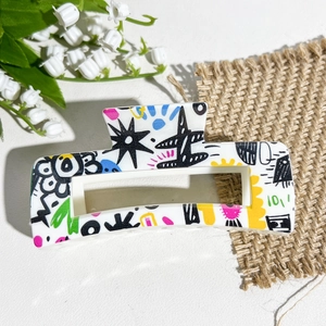 Détail de la pince à cheveux carrée blanche avec graffitis colorés et motifs d'étoiles