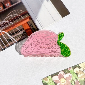 Gros plan d'une pince à cheveux en acrylique en forme de pêche avec feuilles vertes sur fond