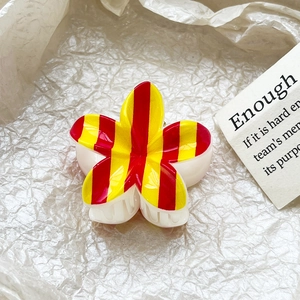 Detail of red and yellow striped flower hair claw clip on a white textured background