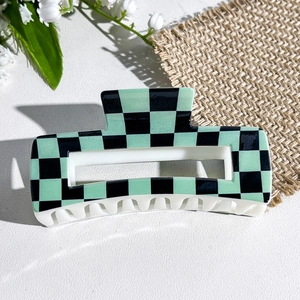 Detailed view of square green checkerboard hair claw clip with white teeth on linen