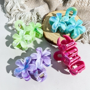 Macro detail of four marble-patterned floral hair claws in acetate on a wooden base
