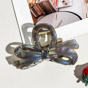 Macro detail of dark grey translucent bow hair claw with pearlescent finish and gold spring