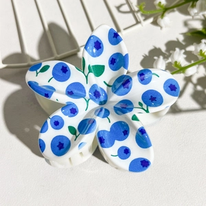 Detailed view of flower-shaped hair claw with blueberry print and white grip teeth
