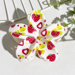 Detail of flower hair claw clip with strawberry print on polished white resin surface