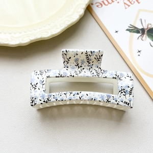 Detail of 8.5cm hollow rectangular hair claw clip with blue floral pattern on cream base