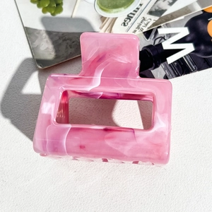 Detailed 45-degree angle of a square pink marble acetate hair claw clip on white leather