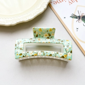 Detail view of a mint green rectangular hair claw clip with delicate yellow floral patterns