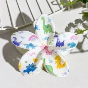 Detail shot of white frangipani hair claw clip with colorful cartoon dinosaur prints