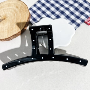Close-up of a large black acrylic hair claw clip with white polka dots and a metal spring