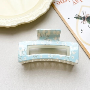Close-up of a light blue rectangular claw clip with white floral patterns on a gray background