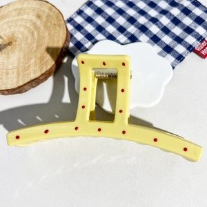Detail view of yellow hair claw clip with red polka dots and metal spring on a tray