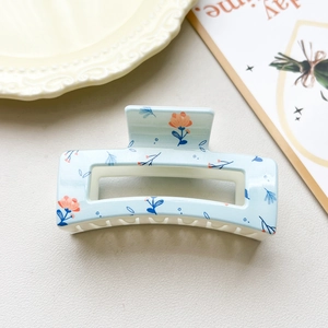 Detail of light blue floral claw clip with orange flowers on a minimalist background