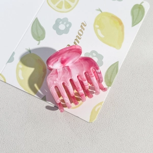 Macro view of pink marble acetate hair claw clip with floral patterns on white background