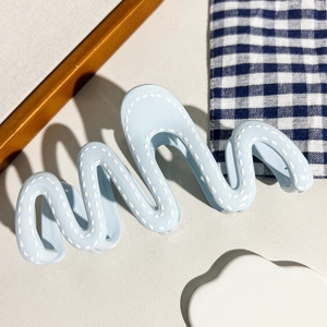 Détail d'une pince à cheveux ondulée bleu clair avec motif surpiqué blanc et fini mat