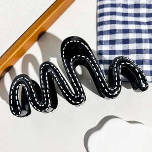 Détail de la pince à cheveux ondulée en résine noire avec motif de couture blanche