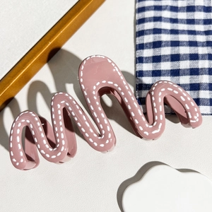 Détail d'une pince à cheveux ondulée rose poudré avec motifs pointillés sur tissu à carreaux