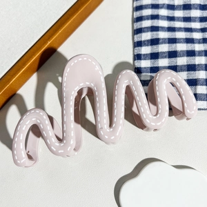 Détail d'une pince à cheveux rose ondulée avec couture blanche sur tissu quadrillé