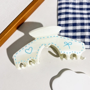Détail d'une pince à cheveux crème avec graffitis de cœurs bleus et bords ondulés