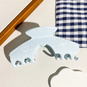 Détail d'une pince à cheveux mate bleu clair avec motifs de cœurs blancs et nœuds